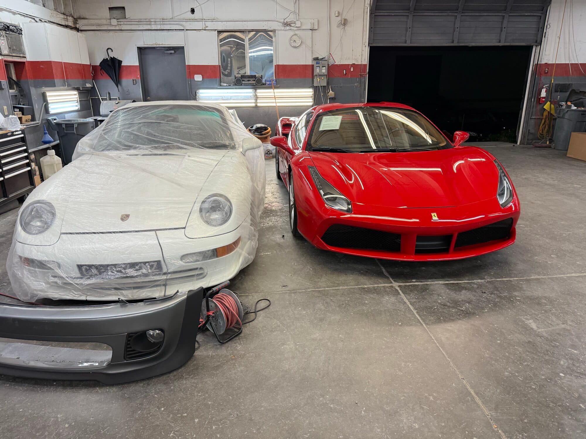A red Ferrari 488 beside a Porsche in for body work at Alpina Auto Body