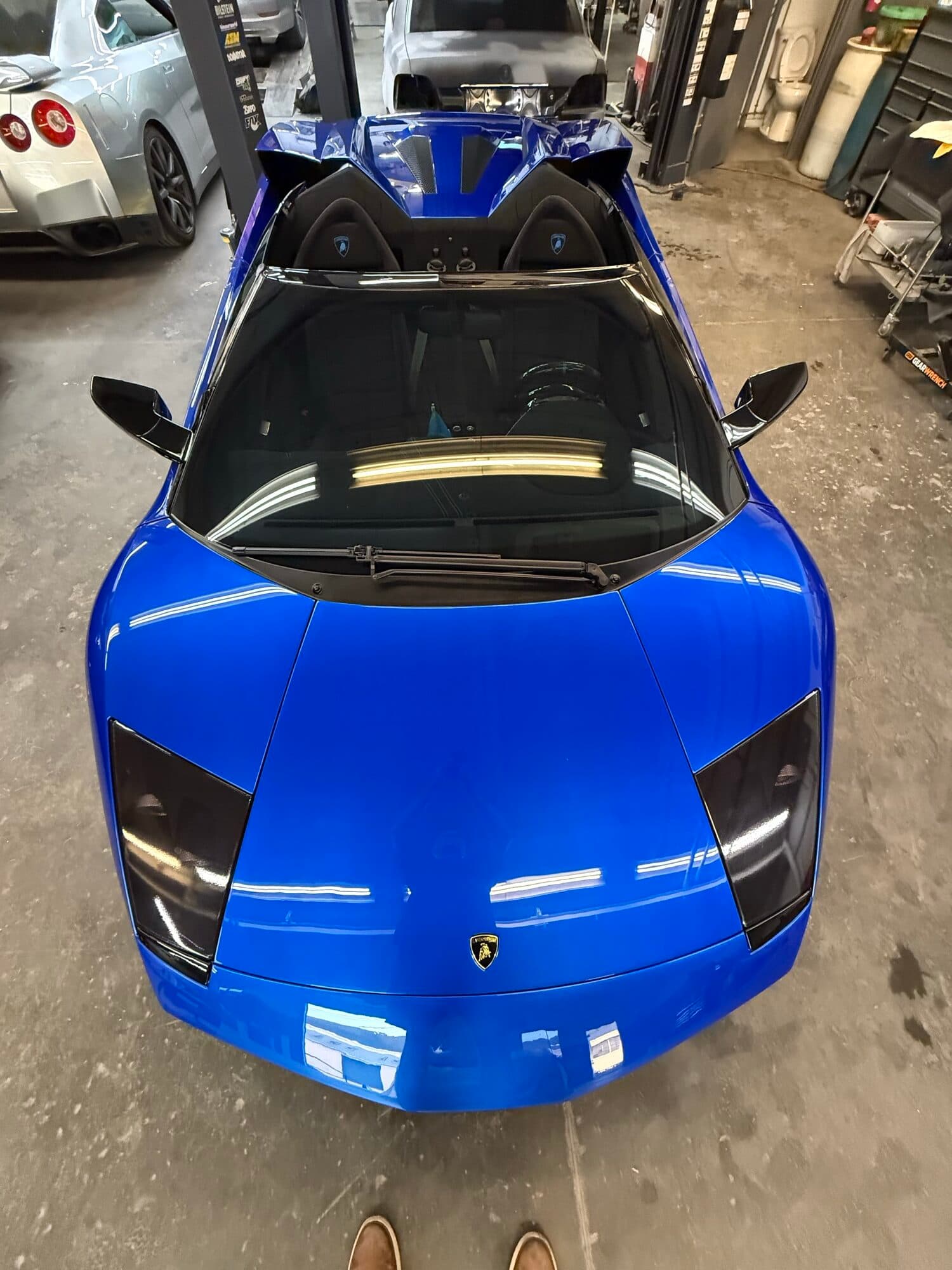 A blue Lamborghini Aventador with an exposed carbon fiber hood in for carbon work at Alpina Auto Body in Southeast Portland