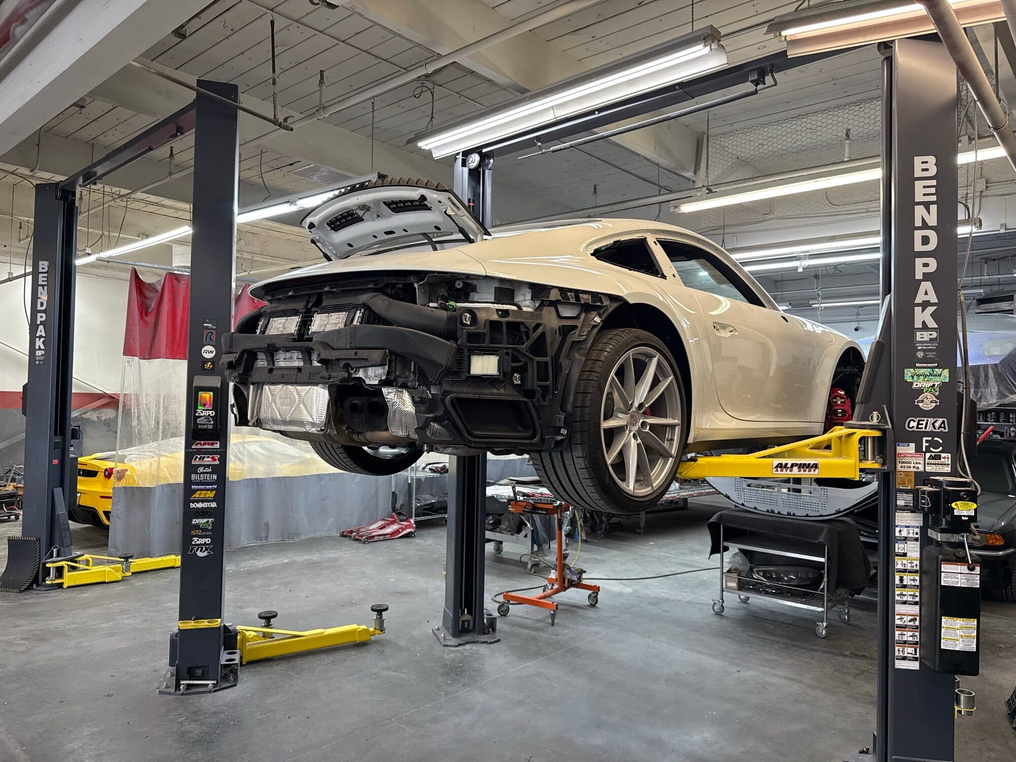 A Porsche on the lift with the front bumper removed during teardown at Alpina Auto Body, Portland