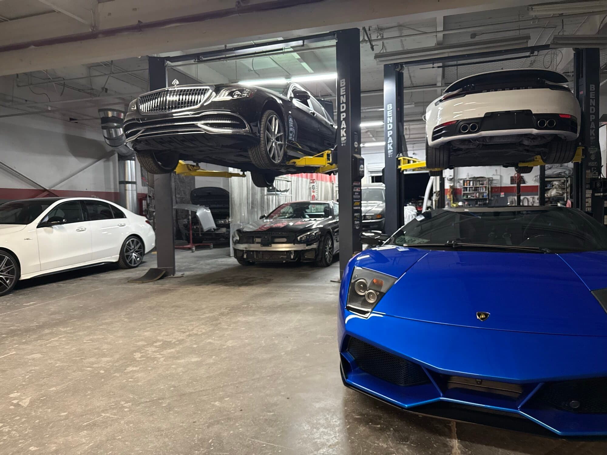 Blue Lamborghini, black Mercedes-Maybach, and a Porsche up on the lifts at Alpina Auto Body, European and exotic body shop in Southeast Portland, Oregon
