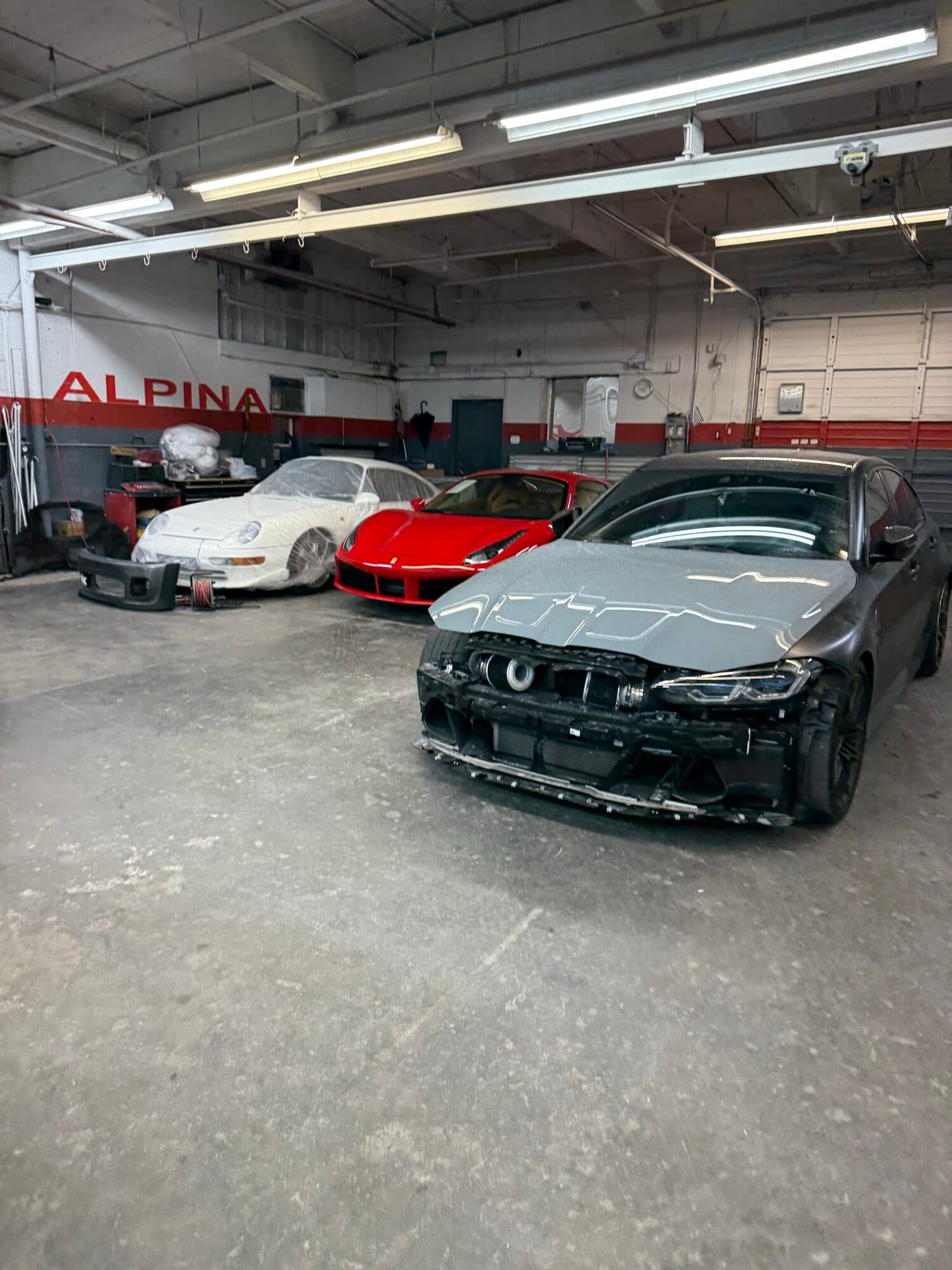 Collision repair in progress at Alpina Auto Body in Southeast Portland: a black BMW stripped down for body work beside a red Ferrari