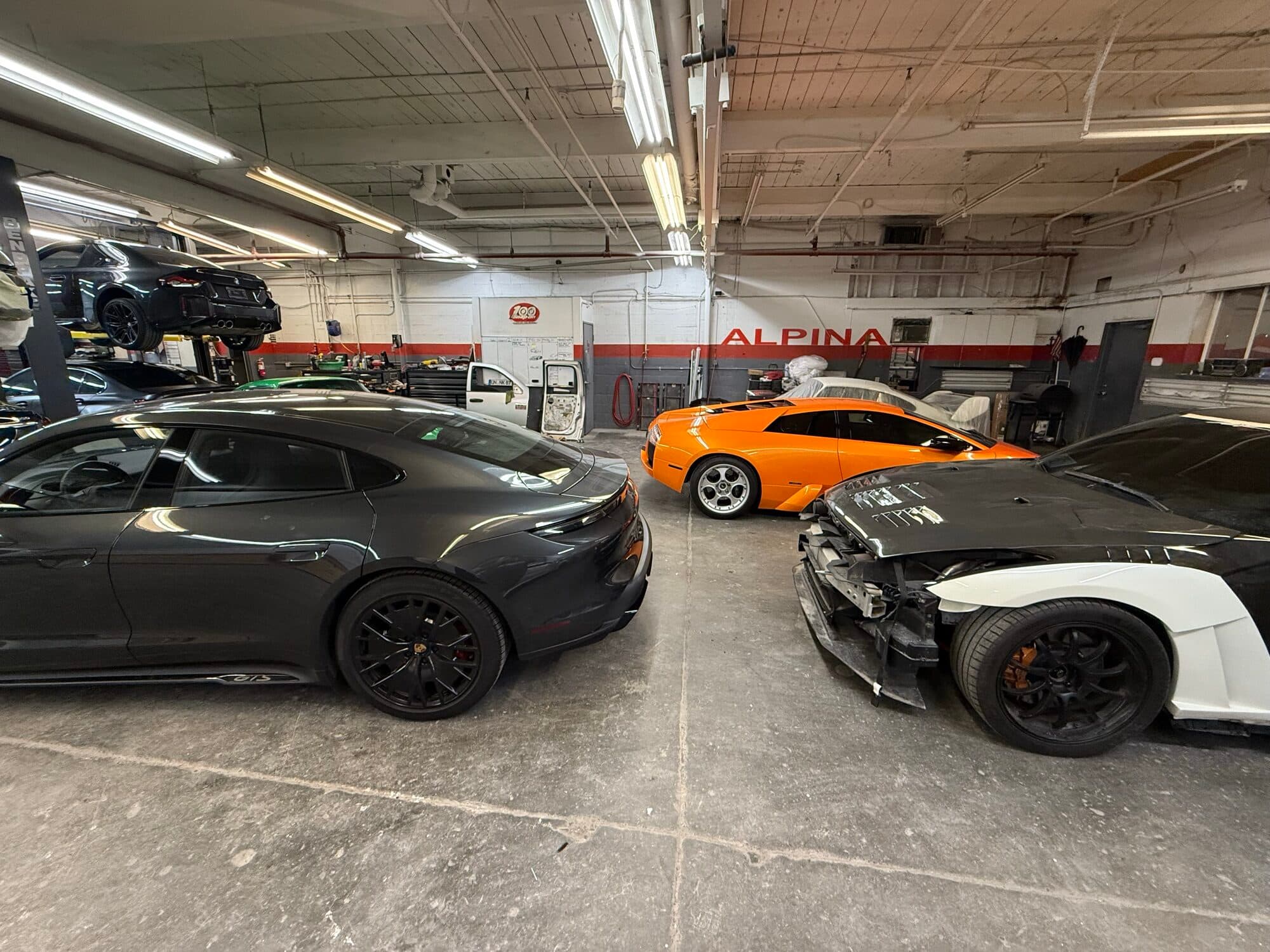 Aston Martin Vantage, orange Lamborghini, and a collision-damaged white Lamborghini on the floor at Alpina Auto Body, exotic collision repair in Southeast Portland, Oregon