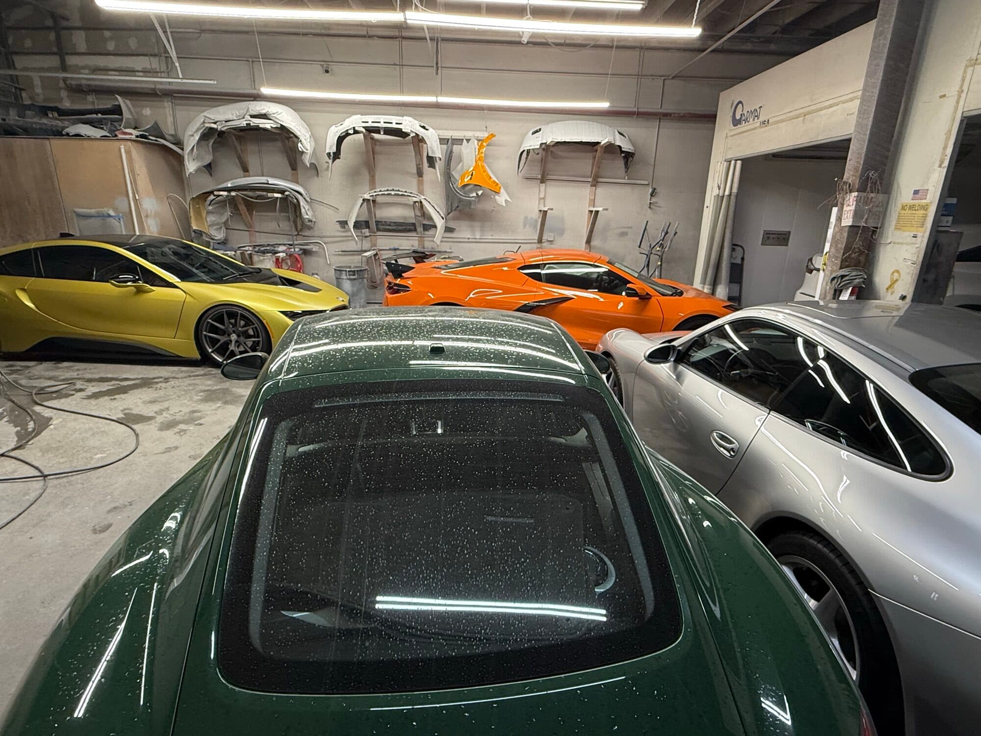 Busy shop floor at Alpina Auto Body with a green Porsche 911, yellow BMW i8, and orange McLaren in for repair, auto body repair shop in Southeast Portland, Oregon