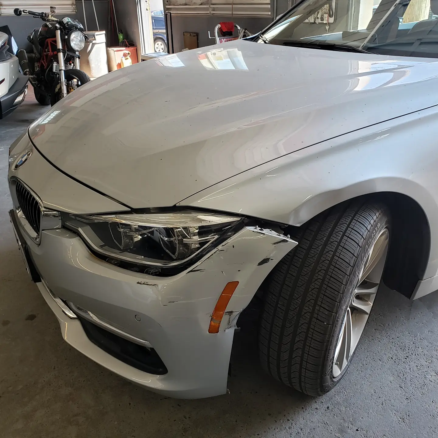 A silver BMW 3 Series with damage to the front fender and headlight before repair at Alpina